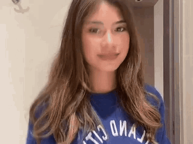 a young woman with long hair is wearing a blue sweatshirt and smiling .