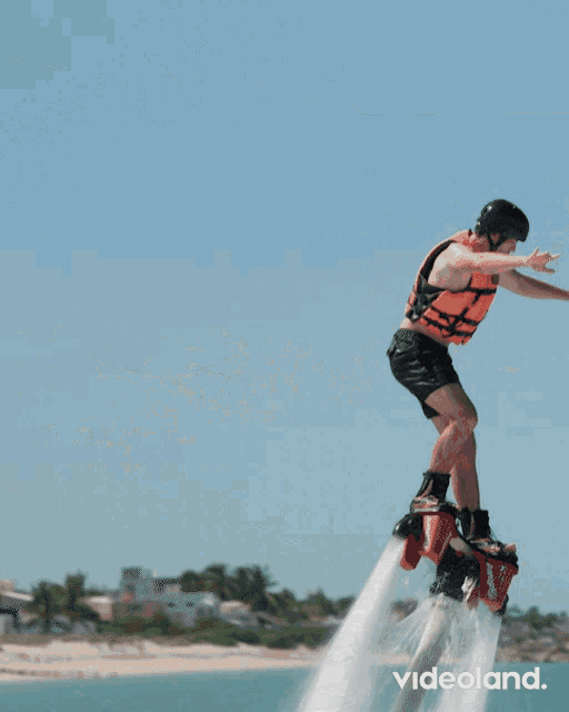 a man in an orange vest is flying through the air on a jet board