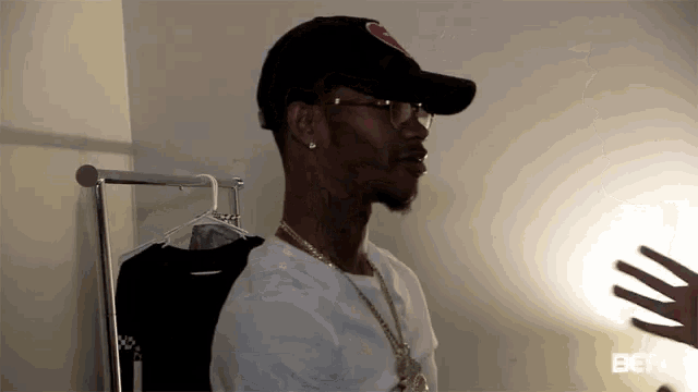 a man wearing a hat and glasses is standing next to a clothes rack