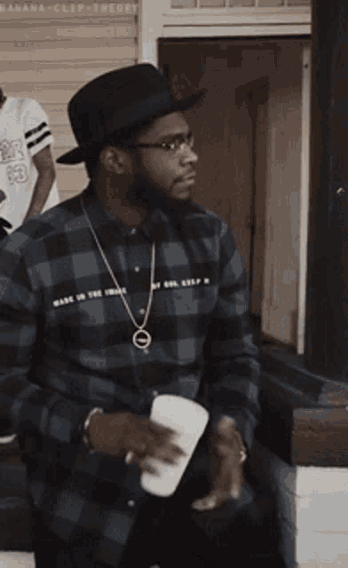 a man wearing a plaid shirt and a hat is holding a cup of coffee