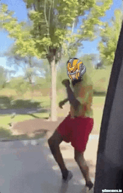 a man in a yellow shirt and red shorts is dancing in front of trees