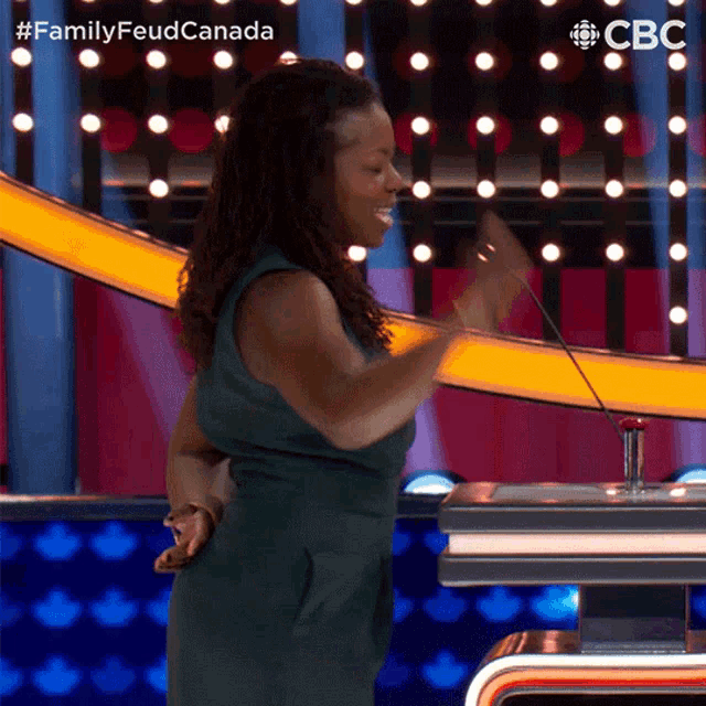 a woman in a green dress is standing in front of a podium with the words family feud canada on the bottom