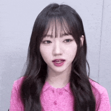 a girl with long hair and bangs is wearing a pink sweater and looking at the camera .
