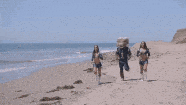 two cheerleaders and a mascot are running on a beach