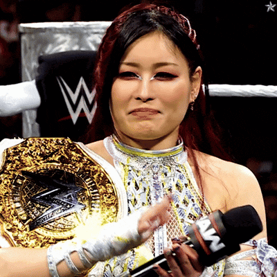 a woman in a wrestling ring is holding a microphone and wearing a wrestling belt