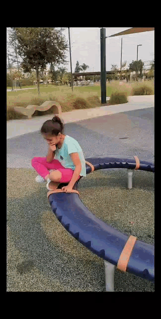 a little girl is sitting on a blue beam in a park .