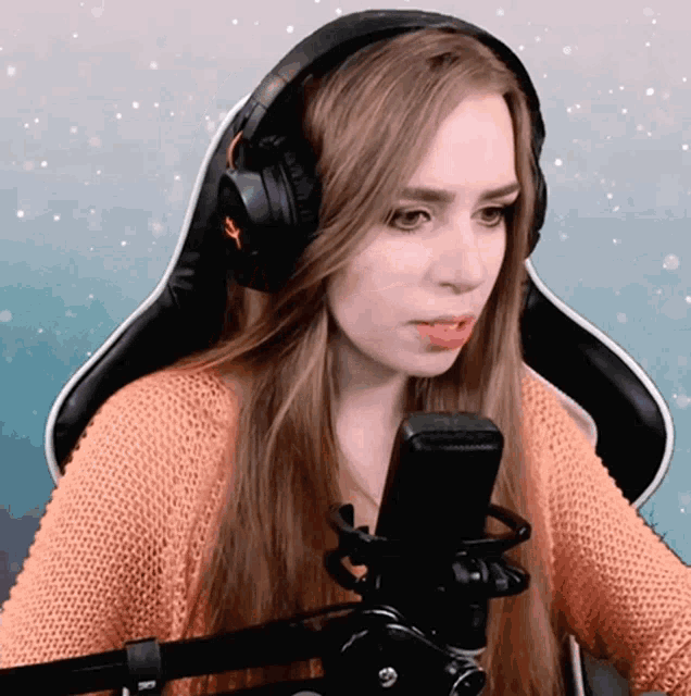 a woman wearing headphones sits in front of a microphone and looks serious