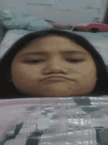 a woman is laying in bed with her eyes closed and making a funny face
