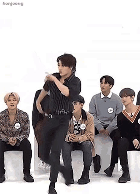 a group of young men are sitting on a couch and watching a man dance .
