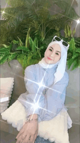 a woman wearing a white hijab and sunglasses is sitting on a couch