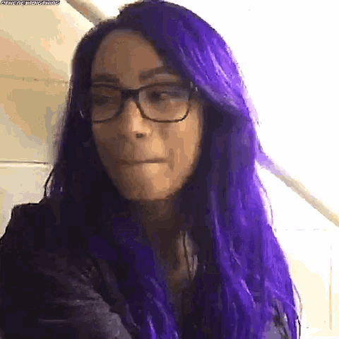 a woman with purple hair is wearing glasses and making a face .