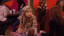 a girl is sitting at a table in a restaurant with other people