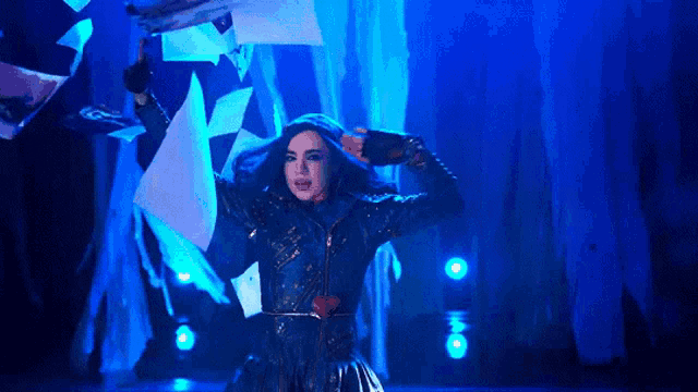 a woman in a blue dress is standing on a stage with papers flying in the air