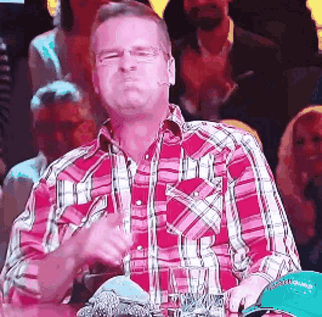 a man in a plaid shirt is sitting in front of a crowd and making a funny face