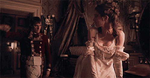 a man and a woman are standing in a room . the woman is wearing a white dress and gloves .