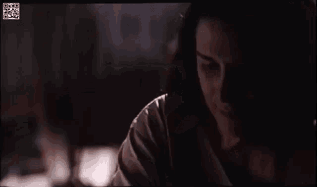 a close up of a woman 's face in a dark room with a qr code on the screen .