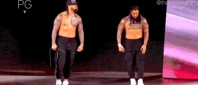 two men are standing next to each other on a stage without shirts on .