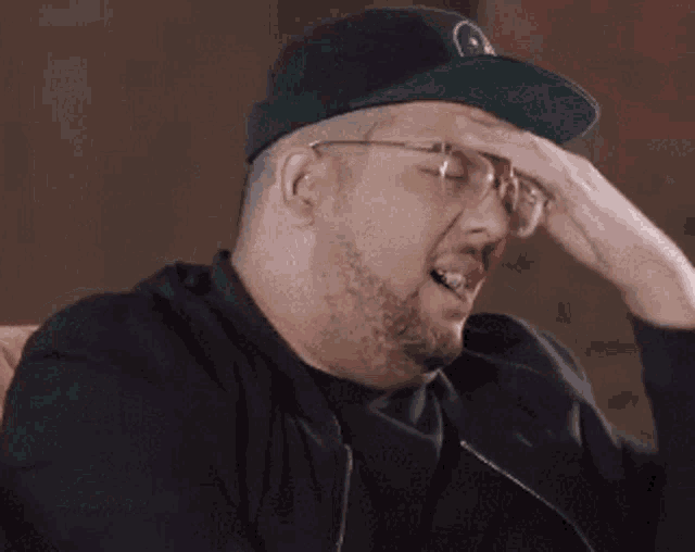 a man wearing a hat and glasses is scratching his forehead .
