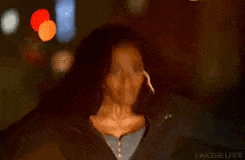 a woman with curly hair and hoop earrings is standing in the dark looking at the camera .