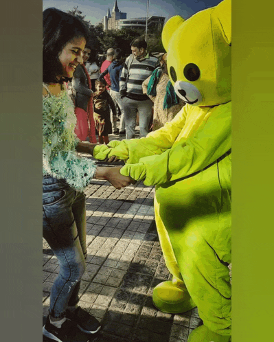 a woman is shaking hands with a yellow teddy bear mascot