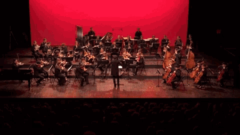 a man in a black suit is leading an orchestra on a stage