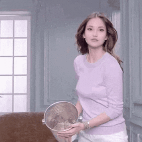 a woman in a purple sweater is holding a bucket of water in her hands .