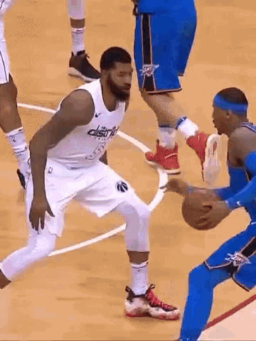 a basketball player is dribbling the ball while another player tries to stop him .
