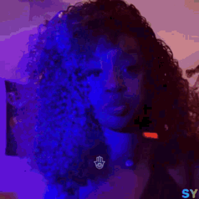 a woman with curly hair is wearing a hamsa pendant