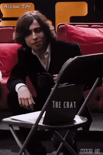 a man in a suit is sitting in a chair with a laptop and a cup of coffee in his hand .