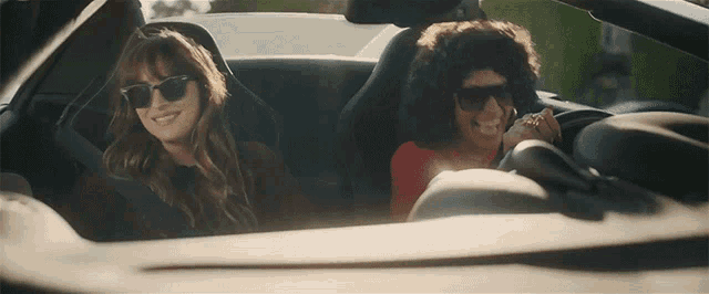 two women wearing sunglasses are driving in a car