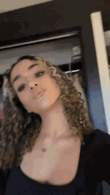 a woman with curly hair is taking a selfie in front of a mirror .
