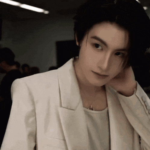 a young man wearing a white jacket and a white shirt is adjusting his hair .