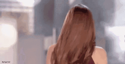 a woman with long brown hair is standing in front of a mirror and looking at the camera .
