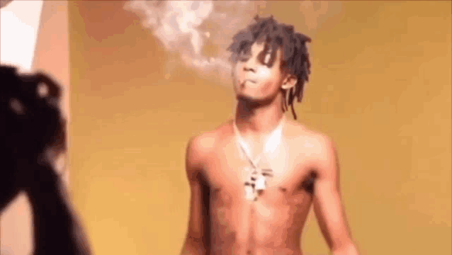 a shirtless man with dreadlocks is smoking a cigarette .