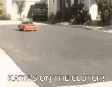 a red rc car is driving down a street with the words katie 's on the clutch .
