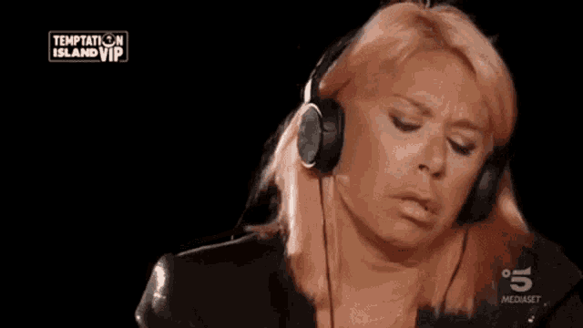 a woman with pink hair is wearing headphones and the words che pochezza pure lui are on the screen .