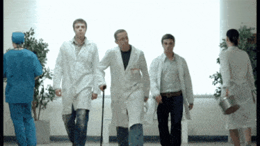 a group of doctors are walking down a hallway with a man with crutches