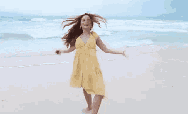 a woman in a yellow dress is running on a beach