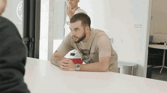 a man sits at a table in front of a wall that says meeting room 02