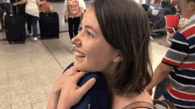 a woman is hugging another woman in an airport while a man stands behind her .