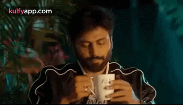 a man with a beard is drinking from a mug .