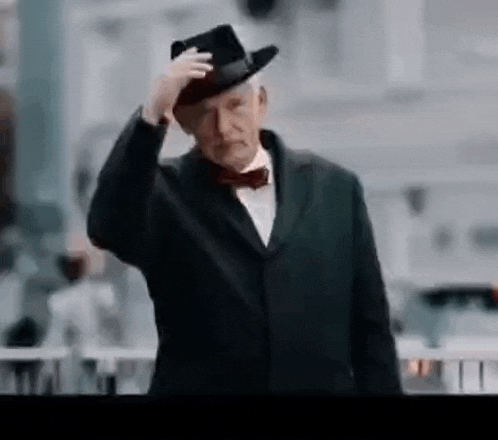 a man in a suit and bow tie is wearing a hat .