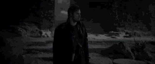 a man in a black coat is walking through a dark cave at night .