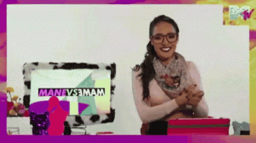 a woman wearing glasses and a scarf is smiling in front of a computer screen that says manevs3mam