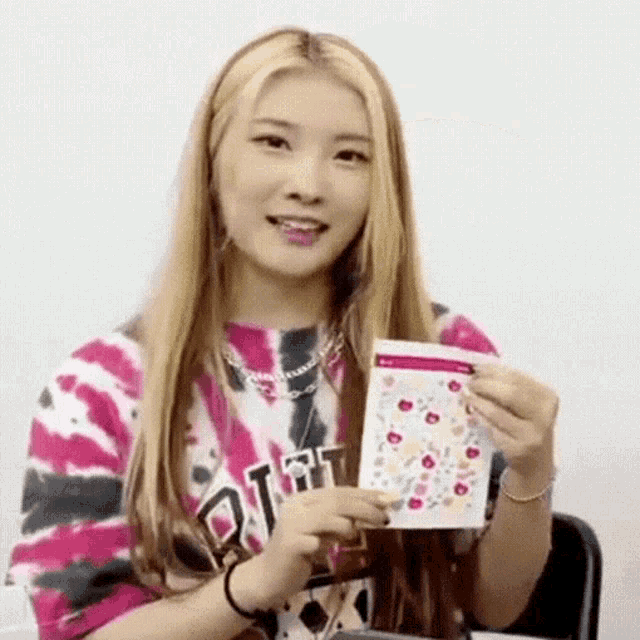 a woman in a tie dye shirt is holding a card in her hands .