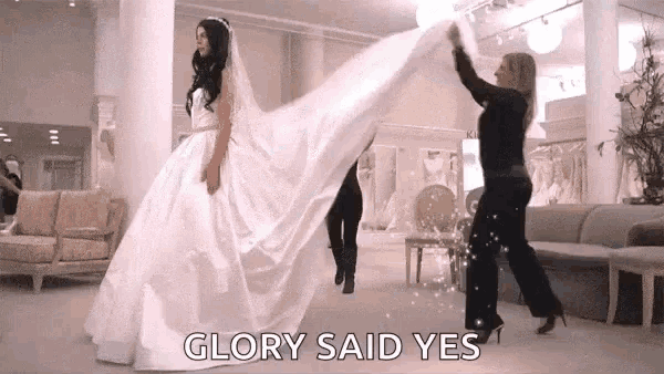 a woman in a wedding dress is being helped by a woman in a black suit who says glory said yes