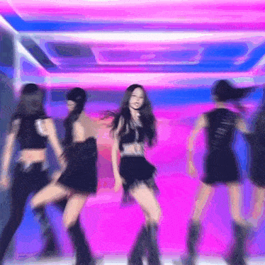 a group of women are dancing on a stage in front of a pink and blue background .