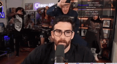 a man wearing glasses stands in front of a microphone in a room with a sign that says dhbspan