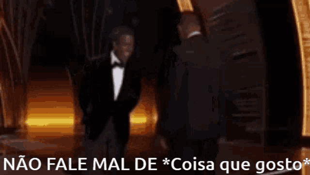 a man in a tuxedo is standing in front of a sign that says " não fale mal de * coisa que gosto "