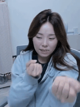 a woman in a blue sweatshirt is making a heart shape with her hands .